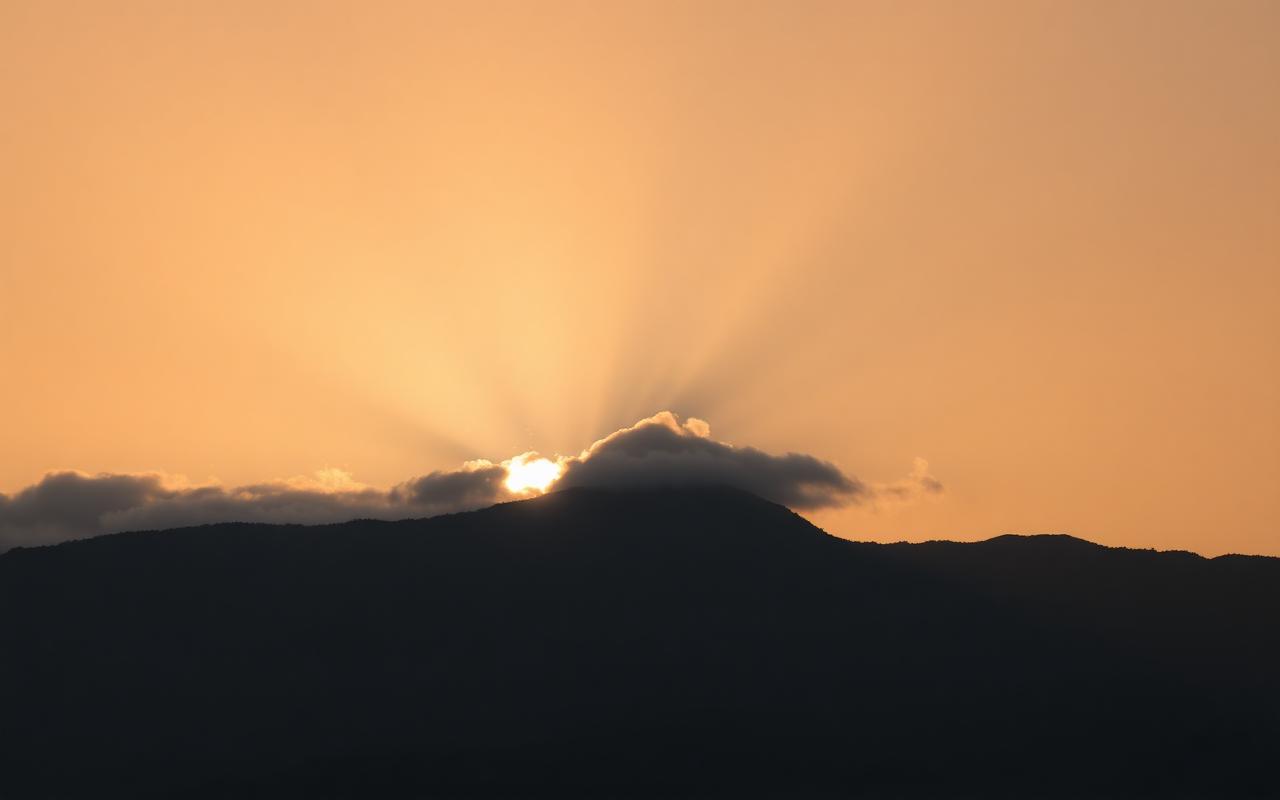 A stark sunrise over a still mountain ridge with a single beam of light cutting through clouds