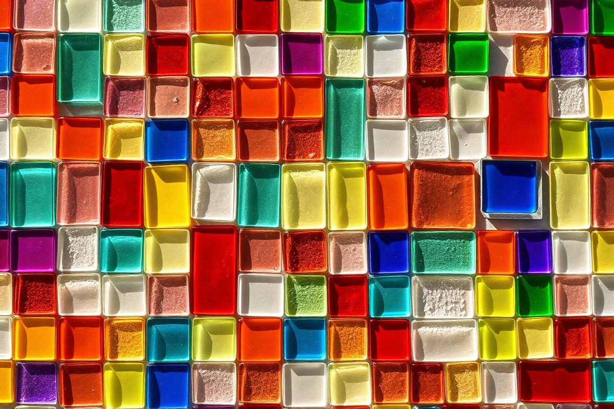 A close up of a colorful mosaic of overlapping translucent glass tiles forming a diverse pattern lit by soft natural light