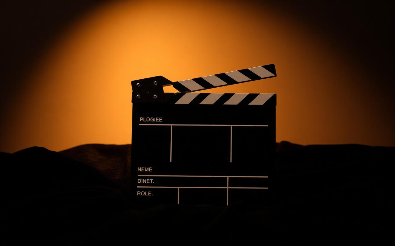 A vintage clapperboard resting on a wooden studio floor beside a coiled length of black cable