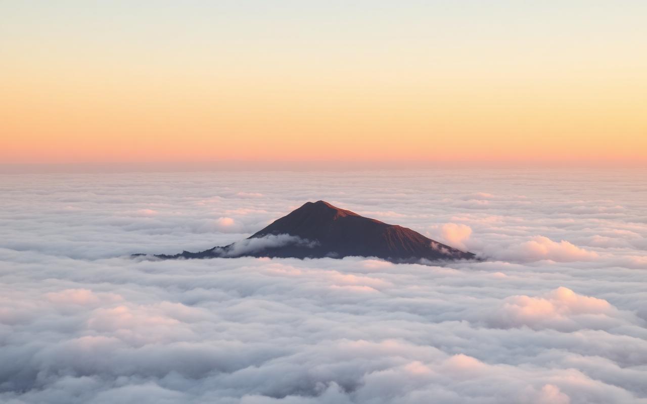A single mountain summit rising above a sea of clouds at sunrise in soft golden light