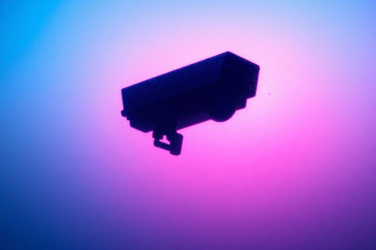 A silhouetted security camera against a soft blue and pink gradient background A silhouetted security camera against a soft blue and pink gradient background