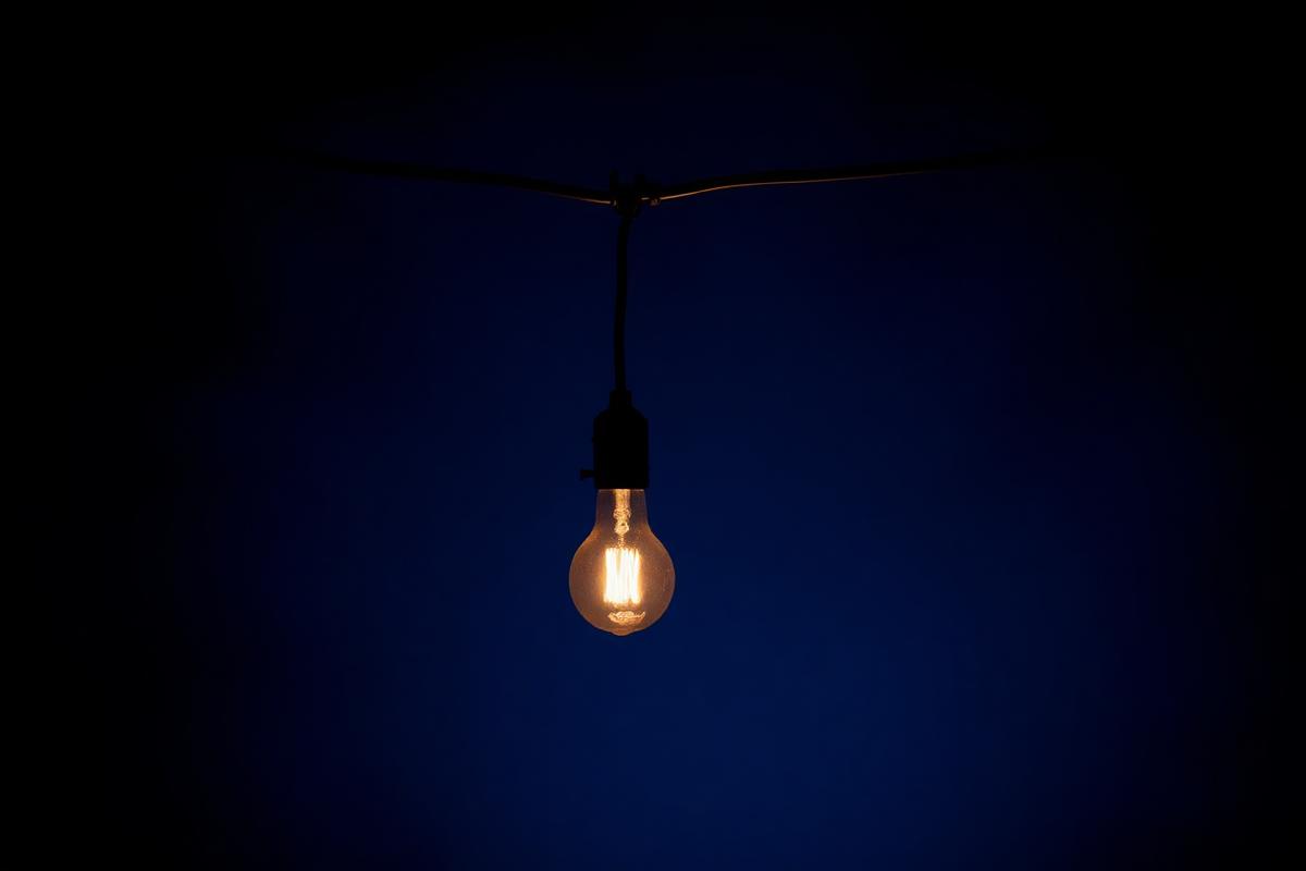 A solitary glowing lightbulb hanging from a wire against a deep dark blue background